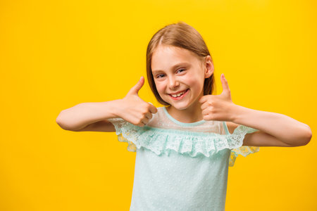 Like and approval. Studio portrait of stylish little children girl gesturing thumbs up and looking at camera. smiling to camera, yellow backgroundの写真素材