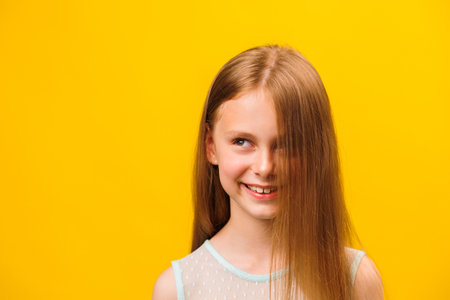 front view of a little girl children with a strand of hair on her face smiling with her teeth. friendly, shy kid posing on yellow studio background.の写真素材