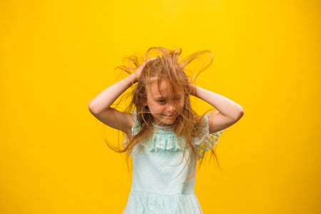 disheveled, kid girl scratch hair on the yellow background, studio shot. scalp problems, tousled and dirty hairの写真素材