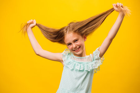Funny girl grimaces in front of the camera. The child holds his hair with his hands. It stands on a yellow background. children and copy spaceの写真素材