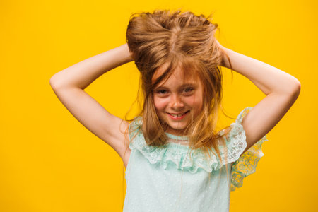 A children with disheveled ruffled hair grabbed her head, Damaged dry kidhair. Isolated on yellow background. dry child hair, unhappy hairy girl.の写真素材