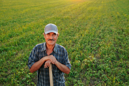 A handsome senior farmer, sporting a distinctive mustache, takes a break amidst the agricultural fields at sunset, his satisfied expression capturing the essence of a days hard work.の写真素材