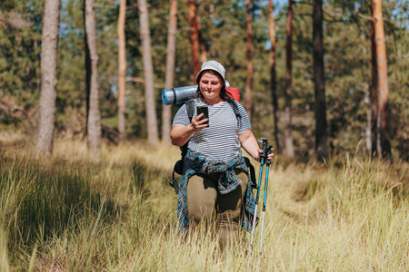 Capture the essence of a solo hiking expedition as an overweight woman takes a break, indulging in smartphone relaxation amidst the scenic woodlands. Celebrate the fusion of technologyの写真素材