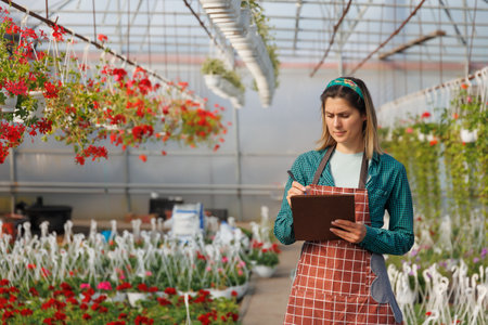 caucasian woman use notebook to analysis and record the data of color flowers, experiment in the Greenhouse. american agronomical engineer inspection the plants in the greenhouse, copy spaceの写真素材