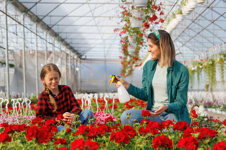 Mother wetting his daughter having fun while working in greenhouse. happy family of flower growers, happy kid and woman playing and having fun togetherの写真素材