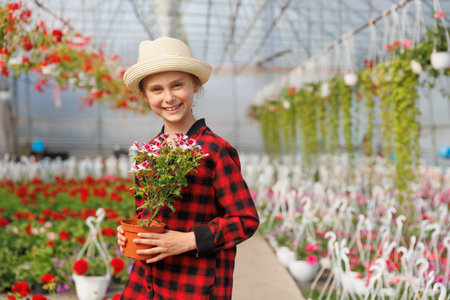 pretty caucasian young smiling preteen kid girl with flowers in greenhouse. glad child looking at camera, Concept work in the greenhouse. Copy spaceの写真素材