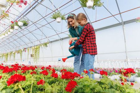 happy Mother and daughter watering flowers in the greenhouse. Beautiful young woman with her daughter watering the plants in the greenhouse.の写真素材