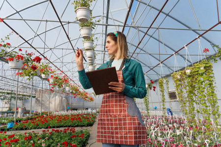 Adorable florist girl working in the greenhouse while holding the notebook. woman analyzes flowers, florist gardening specialist, copy spaceの写真素材
