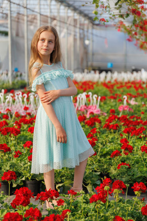 A nice kid girl thoughtfully stands in a greenhouse. Child is wearing a turquoise dress. Kid stands in a thoughtful pose.の写真素材