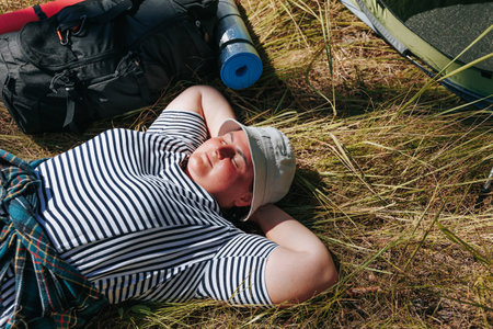Escape into the tranquility of nature with an overweight female hiker, embracing recreation and relaxation on a trekking adventure. Watch as she sits comfortably beside her backpack and tent, enjoyingの写真素材