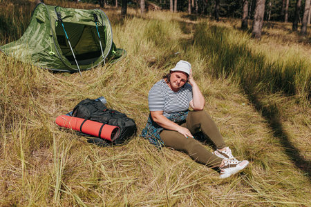 Explore nature with an overweight woman as she discovers moments of tranquility during her hiking adventure. Witness serene scenes by her tent and backpack, embodying the freedomの写真素材