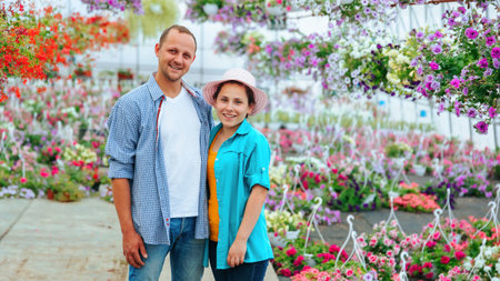 Young happy man and woman rejoice at their success while standing in a greenhouse with flowers. Big glasshouse and next to each other. Young people are dressed in casual style.の写真素材