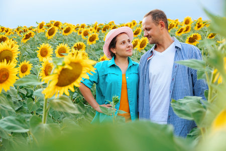 Young people farmers a guy and a girl are standing in a field with sunflowers and smiling happy. There is hat on the girls head. Both are wearing shirts. They are young agronomists. Sunflower and copy space.の写真素材