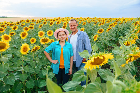 Young people farmers a guy and a girl are standing in a field with sunflowers and smiling happy. There is hat on the girls head. Both are wearing shirts. They are young agronomists. Sunflower and copy space.の写真素材