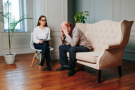 Psychologist woman and sick senior man sit in large cozy office. Man is sick with senile dementia and receives right help. Aging, developmental psychology, gerontology.の写真素材