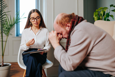 Young woman psychologist tells something to her client to elderly man who props his head with his hands. problems of elderly, help of psychologist, psychotherapist, psychology of aging.の写真素材