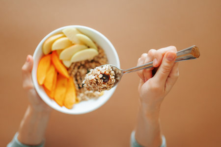 Close up spoon with granola in female hand unrecognizable. Nearby pieces of raw fruit and dried fruit. The concept of healthy food and diet. easy and delicious.の写真素材