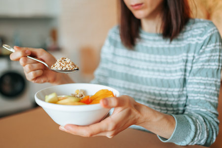 Serious meal, vegan food, young woman holding a spoon with a beautiful appetizing granola and a plate of fruit in her hands. It is good in your home, we monitor our health and get rid of excess weight.の写真素材