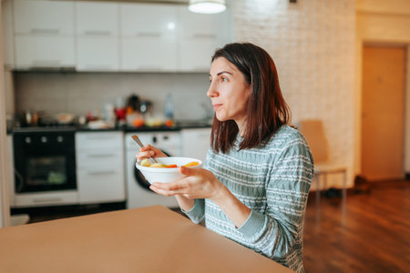 Side view of a young woman sitting at a table with a plate of morning healthy food in her hands, looking into the distance. the girl will take care of her food.の写真素材