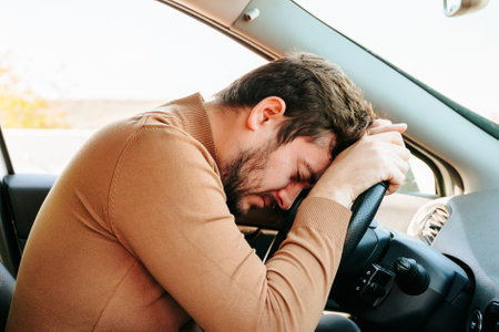 A young driver of a car sleeps at the wheel, hands on the steering wheel, head lies there. Too much time on the road leads to fatigue. You cannot work overtime.の写真素材