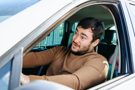A good mood accompanies a young guy on a long journey behind the wheel. The driver is happy to sit behind the wheel of his own car and do what he wants.の写真素材