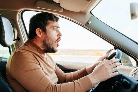 A grimace of surprise, anger and rage on the face of a male driver sitting at the wheel. A guy expresses very violent emotions while riding a vehicle. Different human emotions.の写真素材