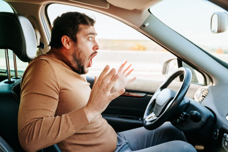 In horror, removing hands from the steering wheel, the young guy screams loudly and bulging his eyes looks ahead. Accidents on the road are always caused by negligence. Sometimes its better to stop.の写真素材