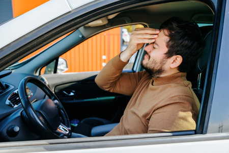young bearded man has a headache, he holds his head in his hand, he is in the car. male who suffers and is unhappy, people ache, desperate people, he is sick, he has painの写真素材