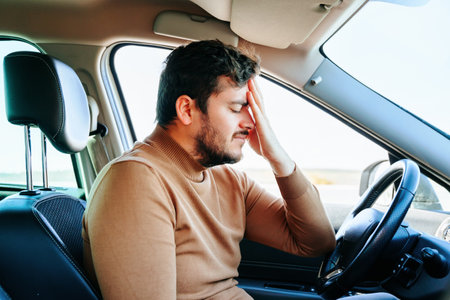 Migraine and headache greatly torment a young man sitting in a car at the wheel. The driver is very upset due to health problems. Beard.の写真素材