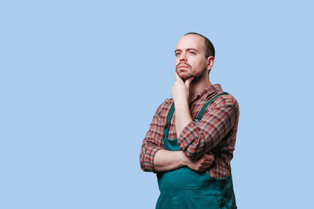 serious, bearded workman exudes an air of contemplation and thoughtfulness in this studio portrait. Dressed in overalls. a pensive young workman seems deep in thought as he gazes off into the distanceの写真素材
