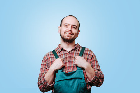 The young, handsome man in the studio shot looks as if he is in the epitome of joy, smiling brightly with a pleased expression, his coverall adding to the overall happy vibe.の写真素材