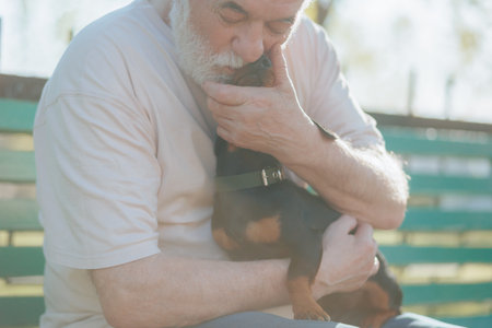 An elderly man, accompanied by his loyal dachshund, enjoys a peaceful moment in the park, showcasing their enduring bond.の写真素材