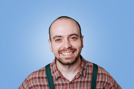 bright and cheerful portrait captures the joy of a happy bearded workman in a studio shot. this young professional exudes positivity and contentment in their overalls and fashionable beard.の写真素材