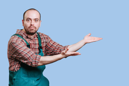 The young man, in his coveralls, has a determined expression as he looks at the camera with his hands spread out, as if hes trying to convey something with his outstretched hands. inquisitive,の写真素材