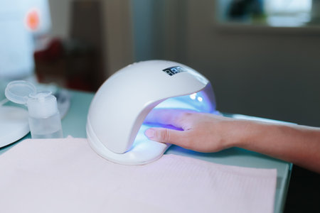 Capturing the essence of nail salon expertise, an image portrays a female hand undergoing a professional manicure treatment, with the ultraviolet nail lamp effectively drying the varnish,の写真素材