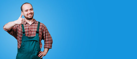 Cheerful handsome builder doing double thumb up gesture with hands and smiling isolated on blue studio background. joyous young man with a beard is seen in this studio, copy spaceの写真素材