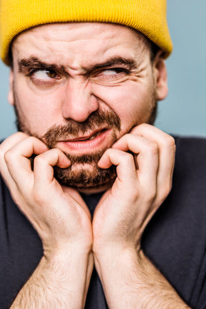 close up portrait, The male has beard itch subject in this studio portrait appears to be feeling uneasy and unhappy studio shot. Distressed man in blue background studio portrait.の写真素材