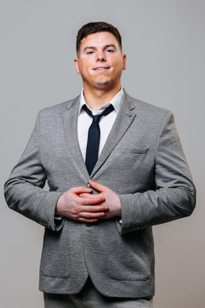 Front view looking at camera young man with vitiligo disease with symmetrical spots on his face. A proud look and love for life characterize strong people. Gray background studio shot business suit.の写真素材