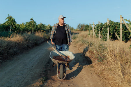 Senior Farmer Pushing Wheelbarrow Along Rural Country Roadの写真素材