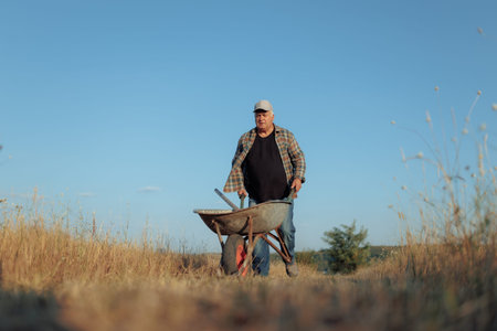 Elderly Farmer Walking and Pushing Wheelbarrow in Countryside
