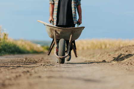 Close-Up of Senior Man Farmer Pushing Wheelbarrow Near Agricultural Fieldsの写真素材