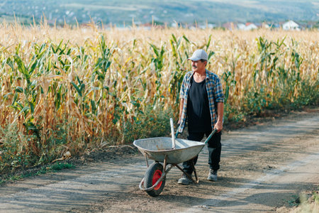 Senior Man Pushing Wheelbarrow Along Rural Path Near Fields