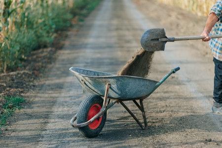 Elderly Man with Wheelbarrow Loading Soil in Agricultural Areaの写真素材