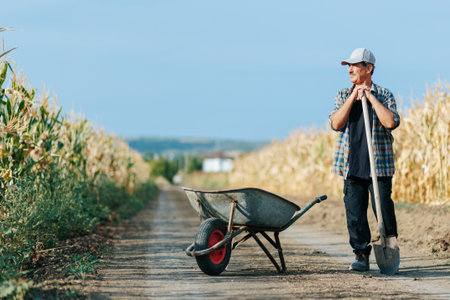 Old Man Farmer with Shovel and Wheelbarrow on Rural Country Roadの写真素材