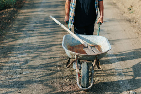 Old Farmer with Wheelbarrow Walking Alongside Farmlandの写真素材