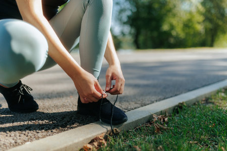 Female athlete tying shoelaces after a fitness workout in the park on a sunny day.の写真素材