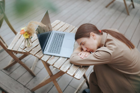 Brunette Businesswoman Facing Exhaustion on the Terrace, Laptop at Her Sideの写真素材