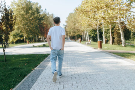 Adolescent boy strolls through a quiet park, hands in pocketsの写真素材
