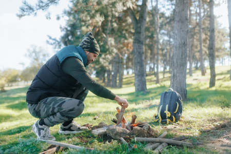A Camper Adds Wood to a Campfire in a Peaceful Outdoor Settingの写真素材