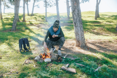 Man Adds Wood to Campfire in Wilderness, Showcasing Survival Skillsの写真素材